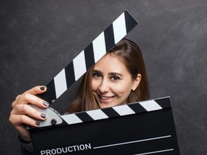 Young woman holding a movie clapboard over black background, studio shot