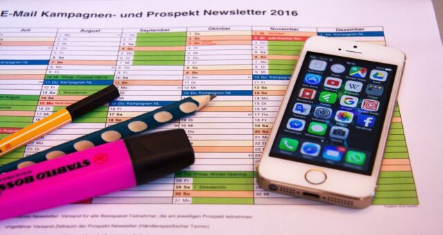 Planering av nyhetsbrev med kalender, pennor och en mobiltelefon.