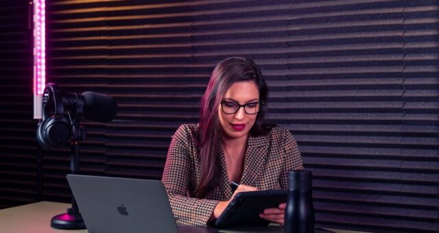 Kvinna antecknar vid laptop och mikrofon i en ljudstudio