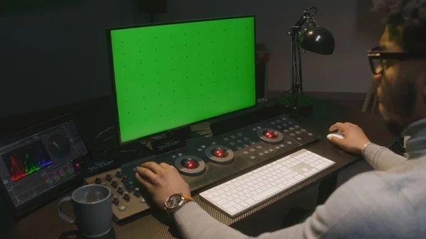 Videotekniker arbetar vid en färgkorrigeringskonsol med grön skärm