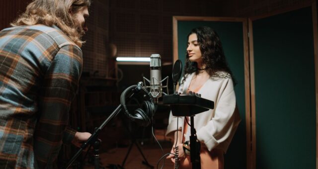 Två personer arbetar med mikrofon och hörlurar i en ljudstudio